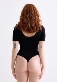 Zwarte aansluitende bodysuit met korte mouwen en een ronde rug, gladde textuur, hoge beenopeningen en opvallende rugdetails.