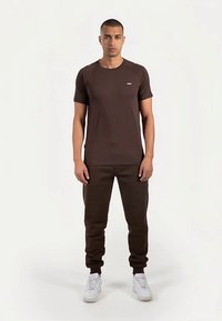 Brązowy t-shirt z krótkim rękawem i okrągłym dekoltem, w komplecie z dopasowanymi brązowymi dresami, charakteryzującymi się gładką fakturą, oraz białymi trampkami.