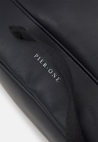 Sac en simili cuir noir avec une texture lisse et un logo "PIER. ONE" en argent bien en évidence. Équipé d'un tirant en tissu.
