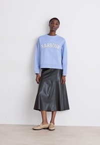 Világoskék pulóver fehér "BARBOUR" felirattal, fekete bőr midi szoknyával és bézs slip-on cipőkkel párosítva.