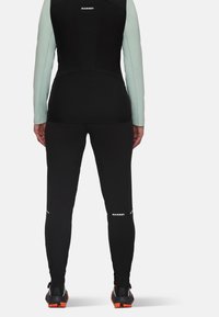 Zwart en groene sportoutfit met aansluitende lange mouwen en broek, met reflecterende details en logoprints. Gelaagd materiaal met rek.