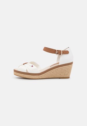 Hvid kile-sandal med tan ankelrem spænde, flettet espadrille-sål og snoet frontrem med lille logo.