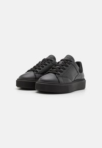 Sneaker in pelle nera con lacci piatti, punta rotonda, suola in gomma testurizzata e design minimalista. Finitura liscia con sottili perforazioni.