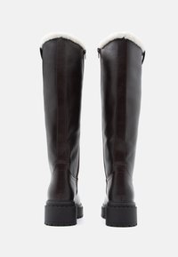 Cizme din piele maro, până la genunchi, cu o căptușeală din lână, fermoare laterale și tălpi din cauciuc groase, având cusături în contrast pentru un plus de detaliu.