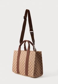 Bolso tote beige y marrón con correa de hombro ajustable, dos asas y patrón repetido de "K" en la superficie del tejido.