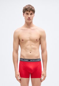 Κόκκινα ανδρικά εσώρουχα boxer από απαλό ύφασμα με μαύρη ελαστική ζώνη μέσης που φέρει το λογότυπο "JACK & JONES". Εφαρμοστή γραμμή, λεία υφή.