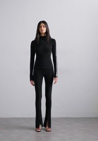 Black turtleneck top and matching pants with split hems, featuring intricate side stitching and a smooth texture. Worn with high-heeled sandals.