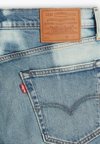 Bolsillo trasero de vaqueros de mezclilla azul claro con la etiqueta roja de Levi's y un parche de cuero marrón con el logotipo de Levi Strauss & Co. sobre el bolsillo.