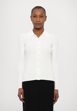 Cardigan bianco a coste, con maniche lunghe e colletto, caratterizzato da una chiusura con bottoni frontalmente e una vestibilità attillata. Tessuto morbido e leggero.