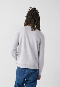 Felpa grigia con maniche lunghe e scollatura rotonda, abbinata a jeans blu. Il tessuto sembra morbido, con polsini e orlo a coste.