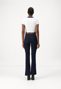 Camiseta blanca ajustada y corta con cuello azul marino, combinada con jeans acampanados de color azul oscuro; textura de denim suave y bolsillos traseros verticales.
