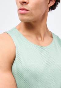 Gros plan d'une personne portant un haut de sport sans manches perforé vert clair avec un petit logo Nike blanc sur la poitrine.