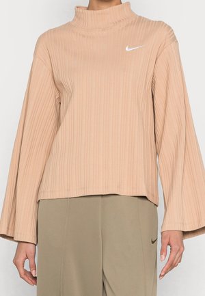 Beżowy prążkowany top z długim rękawem i wysokim kołnierzem z białym logo Nike, w zestawie z pasującymi beżowymi spodniami z małym znakiem Nike.