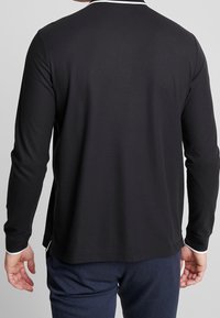 Långärmad svart skjorta i mjukt material med en vit krage. Har rundad nederkant, diskret sömnad och åtsittande ärmar.