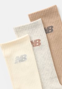 Tri para rebrastih čarapa u krem, svijetlo sivoj i bež boji, svaka s kontrastnim izvezenim logom "NB" na gležnju u drugoj boji.