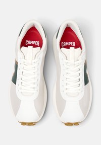 Vita atletiska sneakers med en mesh-textur, med gröna och bruna detaljer, snörningsdesign och röda innersulor med "CAMPER"-logotyp.