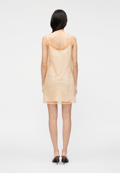 Vestido laranja transparente com corte solto, apresentando um padrão de pontos, alças finas e decote arredondado. Textura de cetim com comprimento até a metade das coxas.