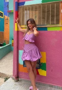 Ensemble deux pièces violet avec des couches à volants et des pois blancs. Comprend une mini-jupe évasée et des accessoires assortis, le tout sur un fond coloré.