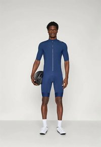 Ναυτικό ποδηλατικό κοστούμι με κοντά μανίκια, διαθέτει μπροστινό φερμουάρ και στενή εφαρμογή. Διακοσμημένο με υφασμάτινη ζώνη στα πόδια, φορεμένο με κράνος.