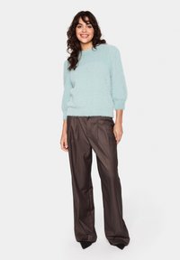 Light teal fuzzy sweater with a round neckline and balloon sleeves, paired with high-waisted, brown wide-leg trousers and pointed black heels.