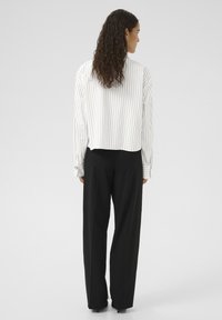 White blouse with vertical black stripes, cropped design, long sleeves with buttoned cuffs, paired with high-waisted black trousers.