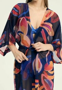 Przezroczysty kimono z żywym, abstrakcyjnym kwiatowym wzorem w odcieniach czerwieni, pomarańczy i niebieskiego. Posiada szerokie rękawy i zapięcie na tasiemkę w talii.