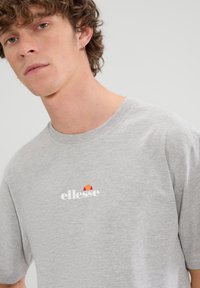 Grijs T-shirt met korte mouwen van een katoenmix. Heeft een ronde halslijn en een logo in wit en rood op de borst. Zachte textuur.