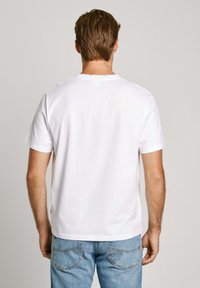 Biała bawełniana koszulka z okrągłym dekoltem, krótkimi rękawami i prostym krojem, w połączeniu z jasnoniebieskimi dżinsami. Brak widocznych wzorów lub grafik.