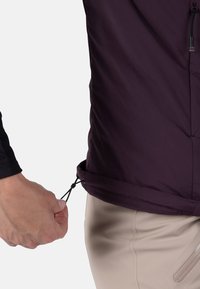 Bordeaux-rotes, leichtes Jackett mit einem taillierten Schnitt. Es hat eine glatte Textur und einen verstellbaren Kordelzug am Saum. Dazu werden beigen Hosen getragen.