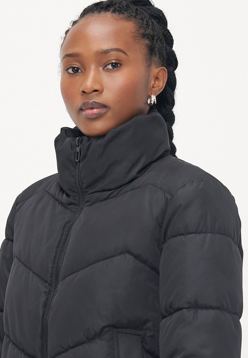 Chaqueta acolchada negra con cuello alto, presenta un cierre de cremallera y un diseño acolchado. Textura suave con costuras visibles y bolsillos laterales.