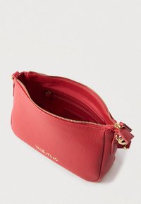 Punane nahast õlakott tekstuurse pinnaga, kuldse luku, sisemiste taskute ja esiküljel reljeefse logoga.