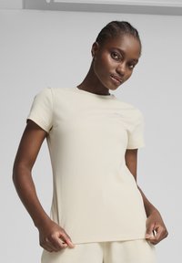 Korte mouwen, geribbelde t-shirt in lichtbeige. Heeft een ronde halslijn en een klein logo op de borst. Materiaal lijkt zacht en rekbaar te zijn.