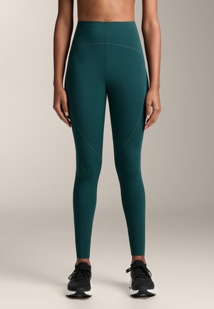 Højtaljede teal leggings lavet af strækbart stof, med en glat overflade, buede sømme og parret med sorte træningssko.