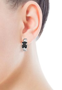 Pendientes de aro en tono plateado con forma de oso negro adornados con pequeñas piedras preciosas, exhibidos sobre un tono de piel claro contra un fondo neutro.