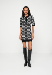 Vestido com padrão preto e branco, com decote de colarinho, mangas curtas e silhueta ajustada, combinado com botas altas pretas.