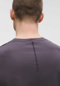 Šedé sportovní tričko s kulatým výstřihem, plochými švy a strukturovanou tkaninou, s jemným šitím po celé délce zad.