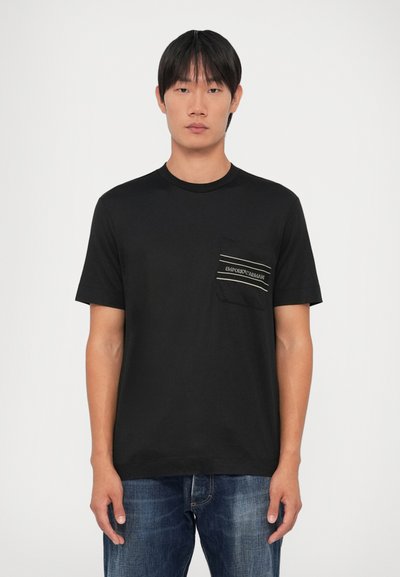 T-shirt preta de manga curta com gola redonda e um bolso featuring um logótipo e detalhes às riscas. Ajuste descontraído, feita de algodão suave.