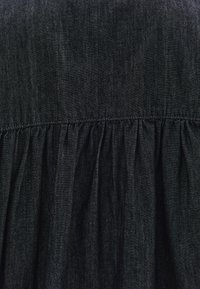 Černé džínové šaty s nařaseným pasem, jemnou texturou a nenápadným leskem. Jednoduchý design bez dalších vzorů či akcentů.