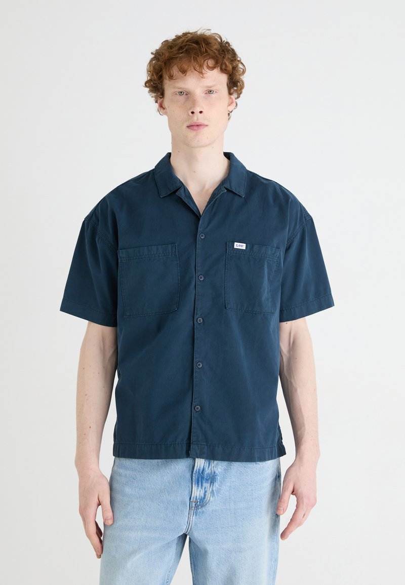 Navy blue short-sleeve shirt with a camp collar, two chest pockets, and button front detail. Made of lightweight fabric with a smooth texture.