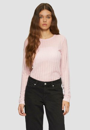 Helles rosa, geripptes Langarmshirt mit Rundhalsausschnitt, kombiniert mit schwarzen Hosen, die Taschen und silberne Knopf-Akzente aufweisen.
