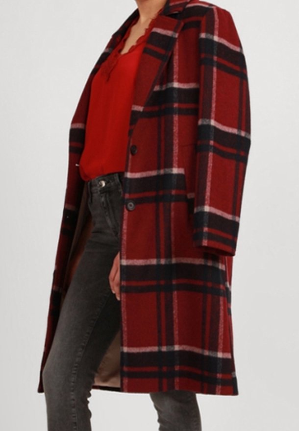 Cappotto di lana a quadri rossi e neri con una vestibilità sagomata, caratterizzato da un revers a incavo e due bottoni, indossato sopra una maglia rossa e pantaloni grigi.