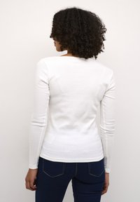 Witte langemouwen fitted shirt met een ronde hals en geribbelde textuur, gecombineerd met donkerblauwe jeans met contrasterende stiksels.