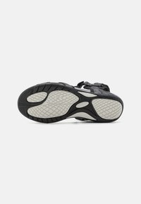 Chaussure de sport noire avec une semelle extérieure en caoutchouc texturé, dotée d'une semelle intermédiaire à motifs et de sangles ajustables sur un dessus en maille tissée.