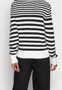 Sweter w paski w czerni i bieli, z prążkowanym dekoltem i mankietami, w luźnym kroju i charakterystycznym poziomym wzorze.