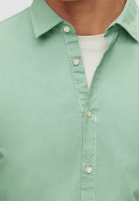 Camicia verde chiaro con bottoni, realizzata in tessuto morbido, dotata di colletto classico, bottoni in plastica e dettagli di cucitura discreti lungo le cuciture frontali.