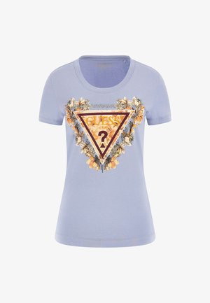 T-shirt bleu clair à manches courtes présentant un graphique floral triangulaire avec le texte "GUESS" et des sequins décoratifs. Matière en coton douce et lisse.
