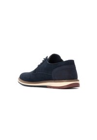 Zapato de ante azul marino con puntera redondeada, diseño de cordones y media suela beige en contraste. Presenta un panel trasero texturizado y suela de goma.