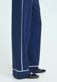 Námořnické široké kalhoty z lehkého materiálu, s bílými kontrastními lemy po stranách a na lemu, spárované s černými lakovanými botami.