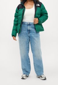 Zelená a černá péřová bunda přes bílý top, zkombinovaná s světle modrými džíny s vysokým pasem a černo-bílými teniskami.