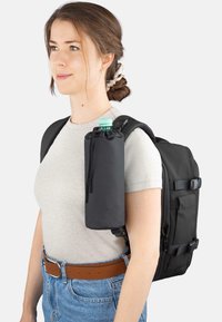 Schwarzer Rucksack mit verstellbaren Riemen, ausgestattet mit einer abnehmbaren dunklen Tasche mit grünem Deckel zum Tragen einer Wasserflasche. Freizeitkleidung.